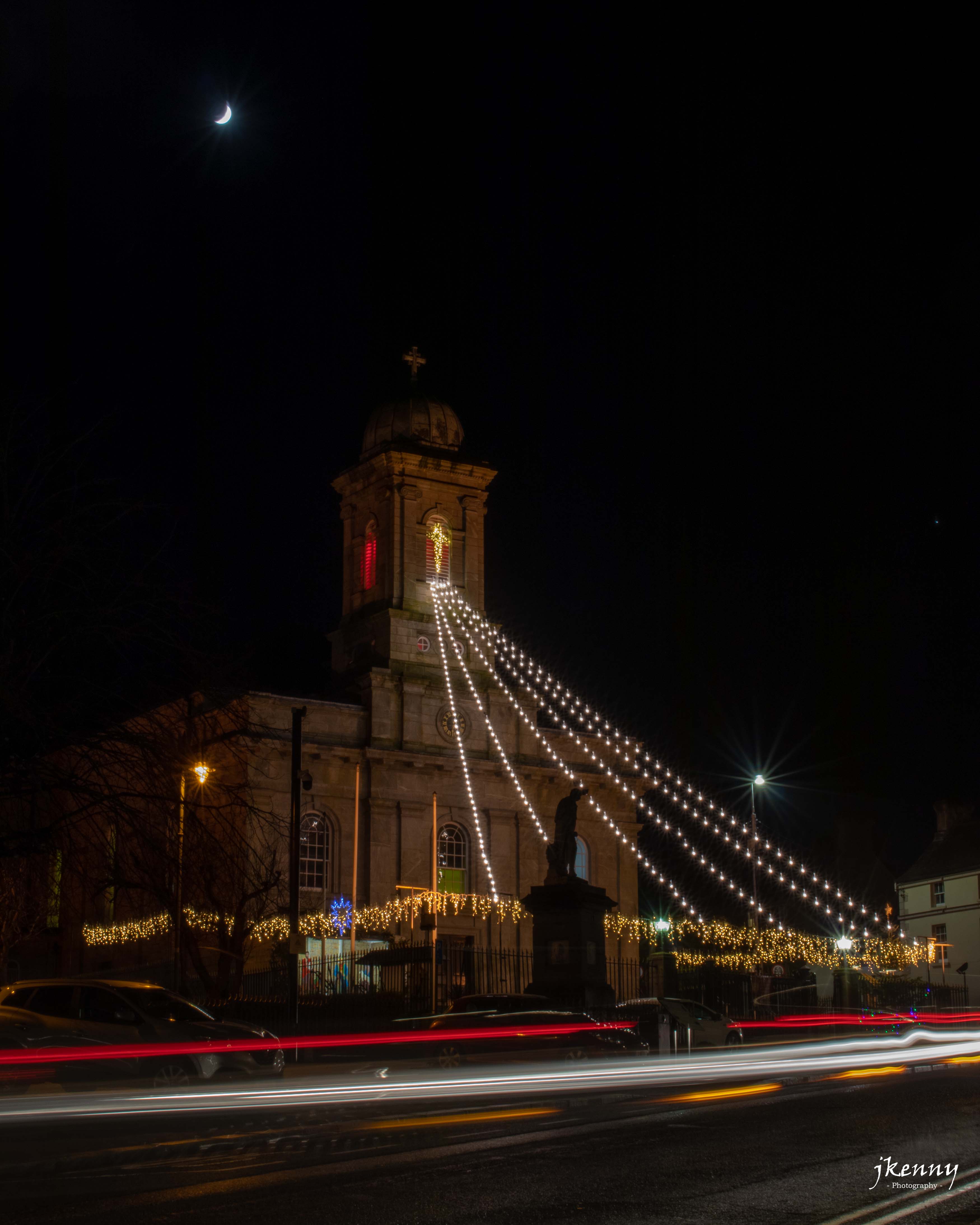 Traffic passing the church with the moon.
